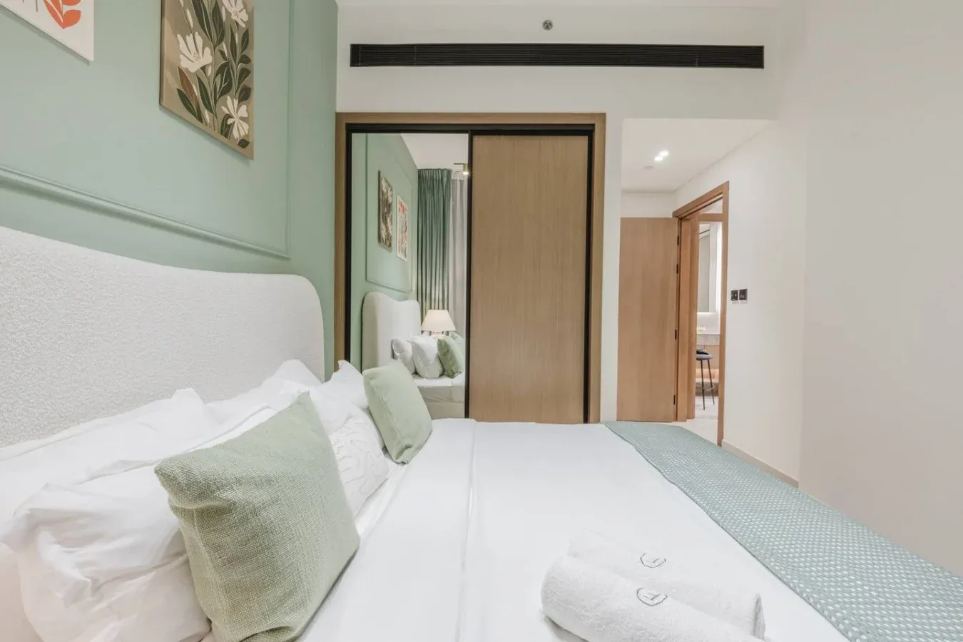 Un dormitorio con una cama bien arreglada, almohadas verde pálido y un armario corredizo.