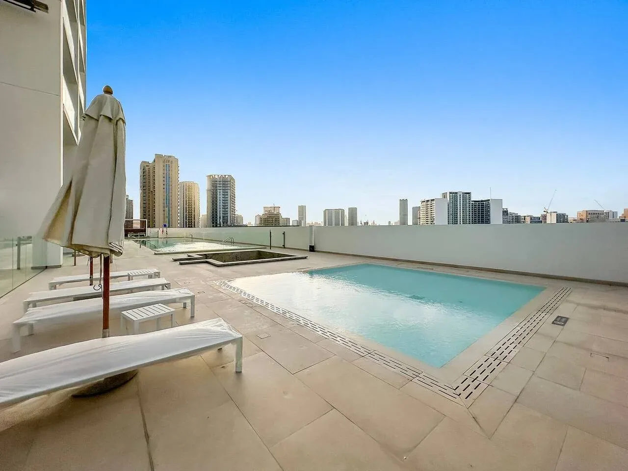 Una piscina en la azotea está junto a asientos de descanso, con edificios de la ciudad al fondo.