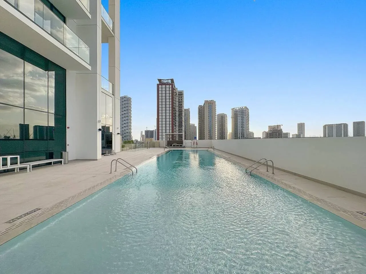 Una piscina en la azotea está junto a un edificio moderno, con torres urbanas a lo lejos.