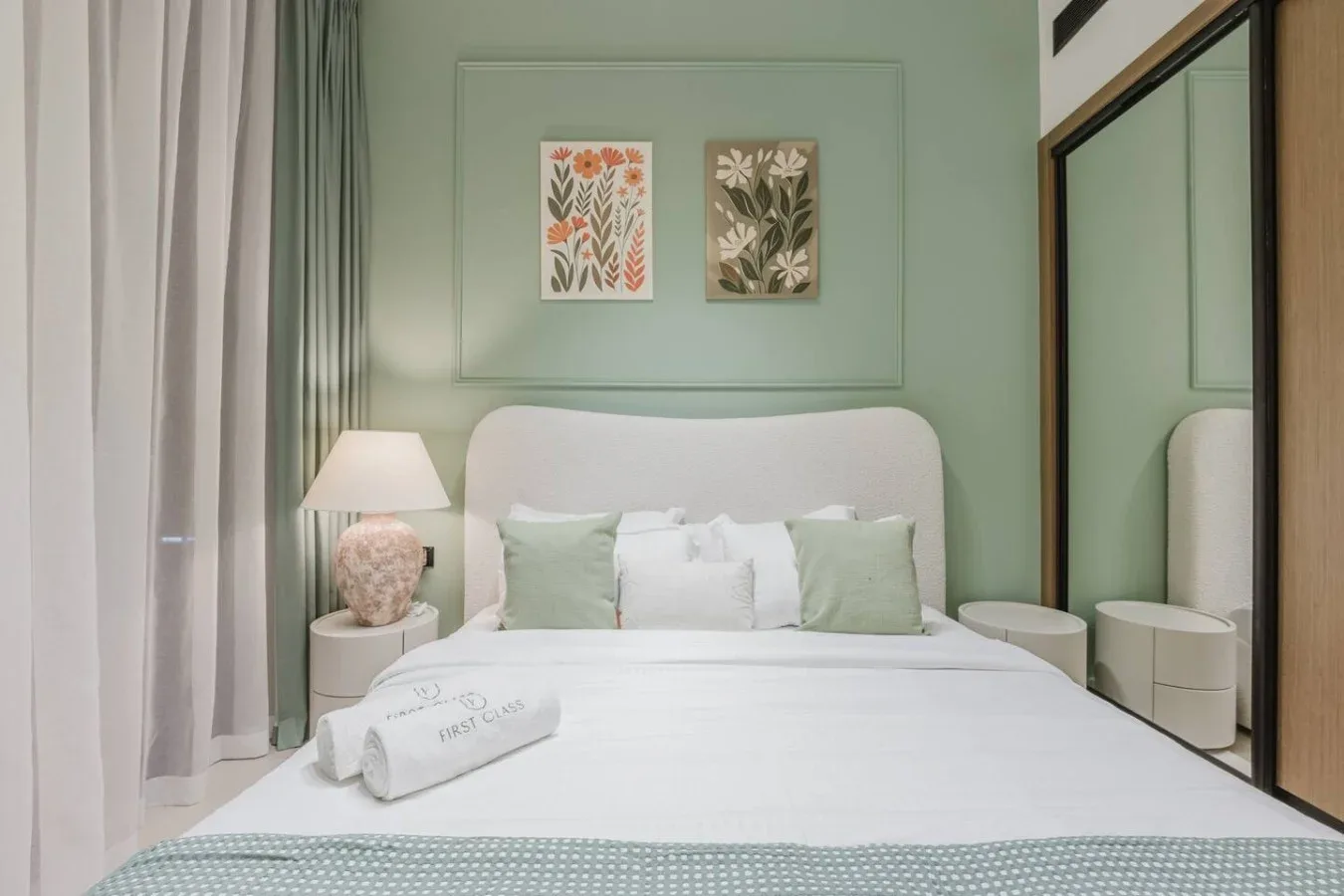 Un dormitorio con una cama bien tendida, paredes verde claro y láminas botánicas.
