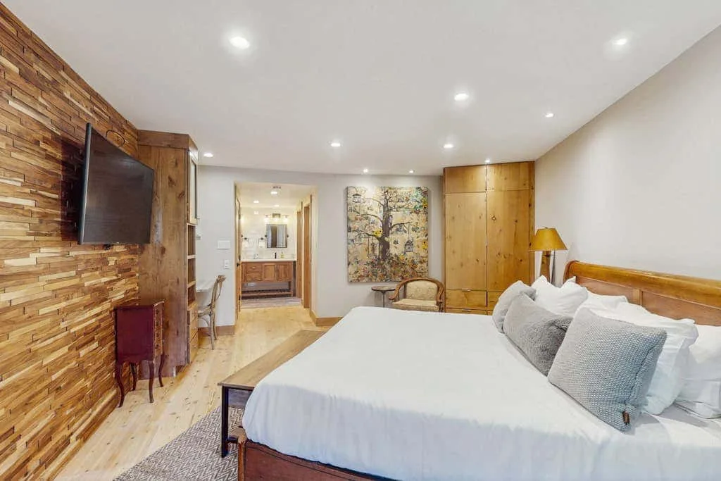 A bedroom with a large bed, wall-mounted television, and wooden cabinetry.