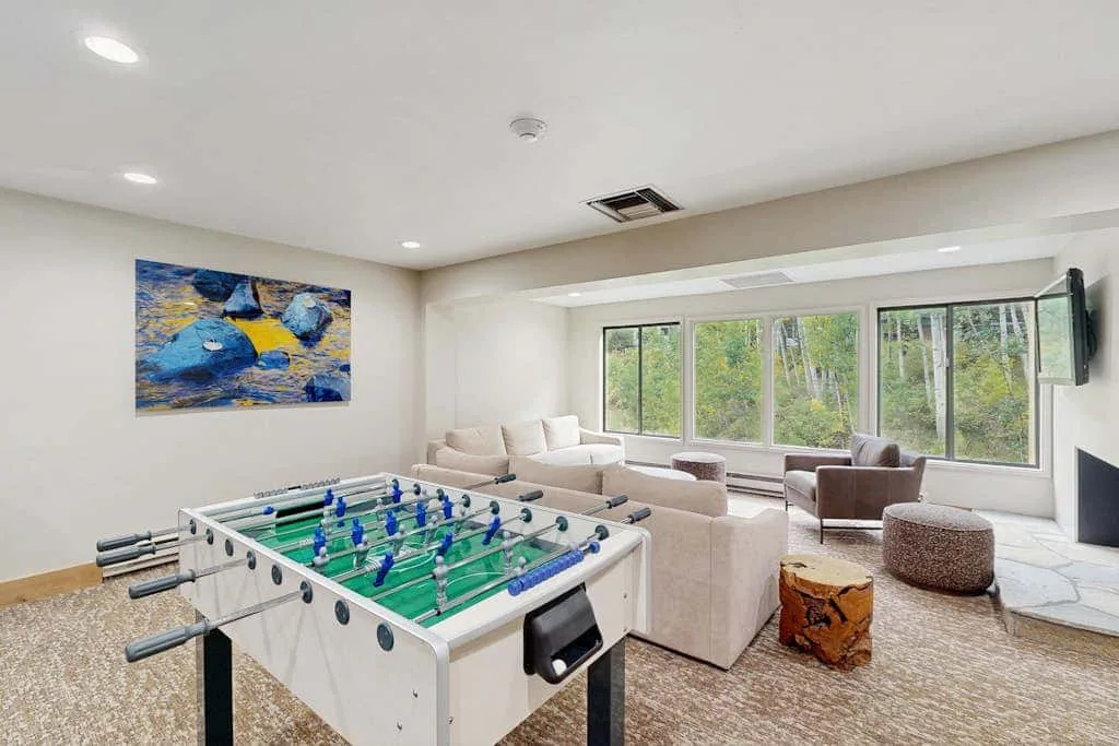 A bright lounge features a foosball table and seating beside wide windows.