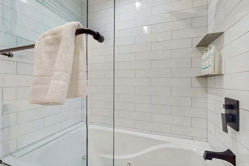A tiled shower with a glass panel, towel, and wall-mounted controls.