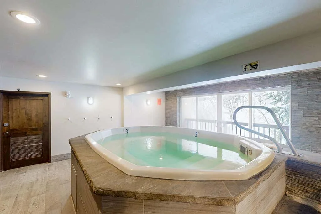 An indoor hot tub sits beside large windows in a tiled room.