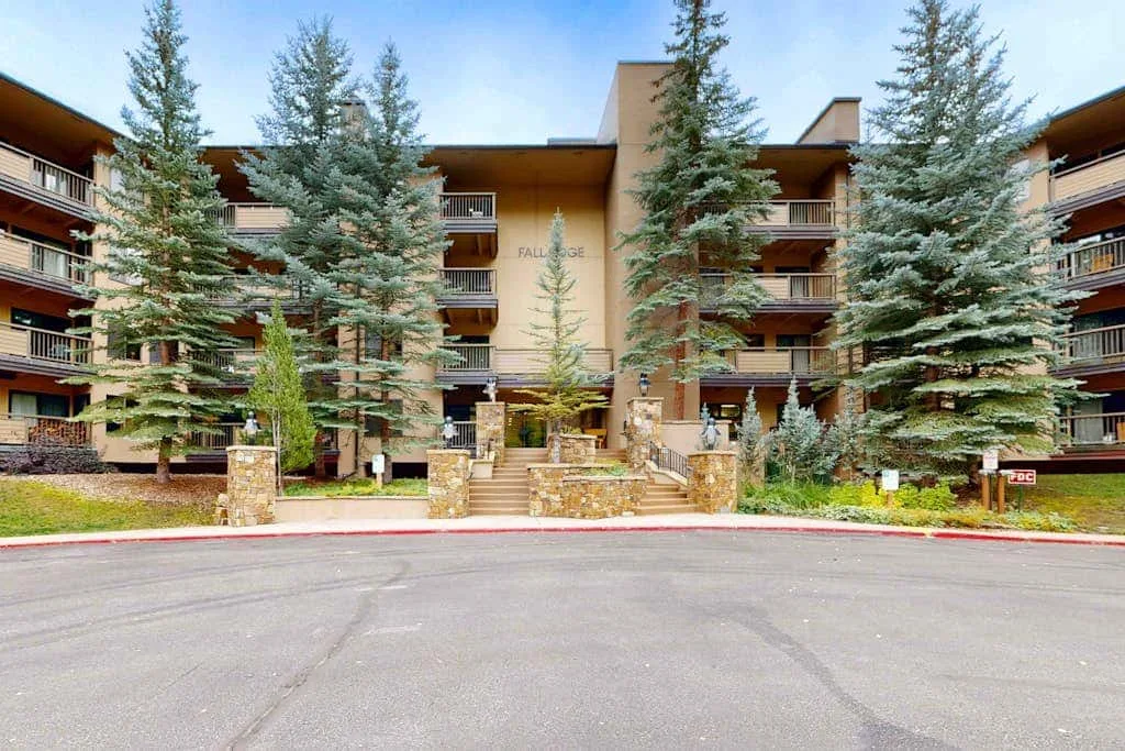 A multi-story building stands behind evergreen trees and a paved driveway.
