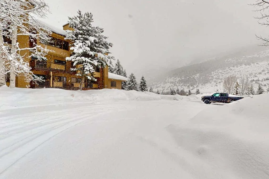 A snow-covered lodge stands beside a broad snowy parking area.