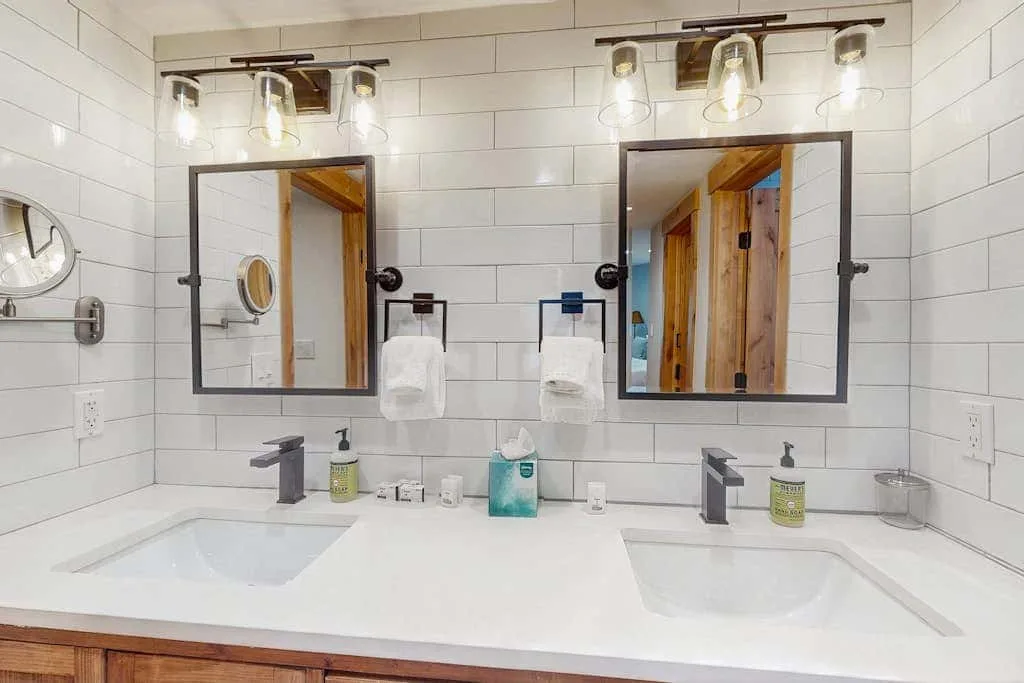 A bathroom vanity with two sinks, mirrors, and bright wall lights.