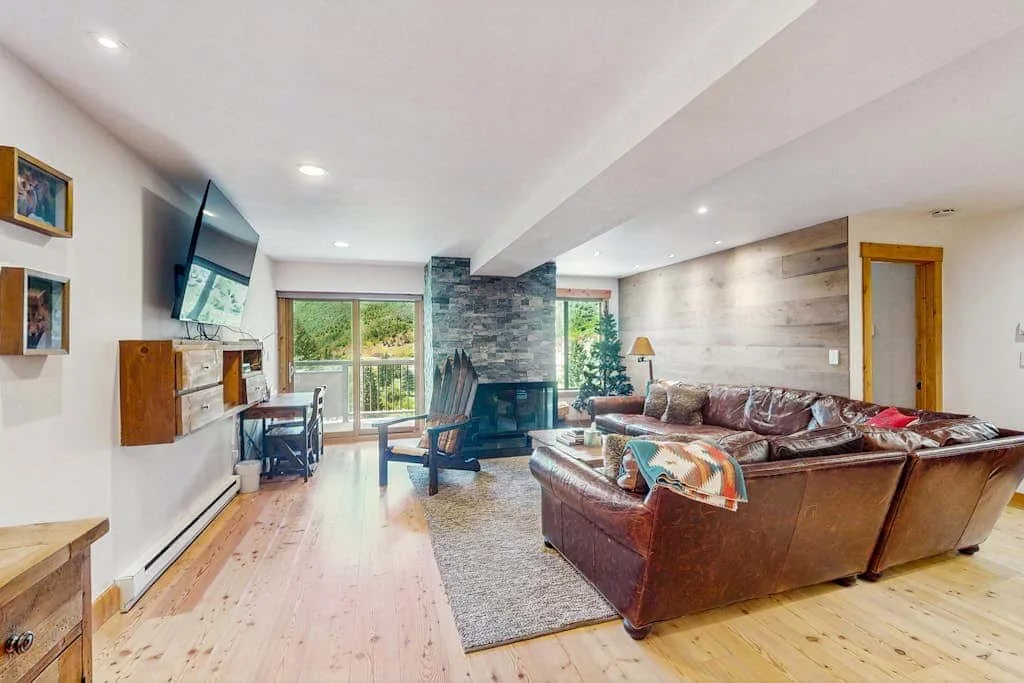 Living room with leather seating, a fireplace, and windows overlooking greenery.