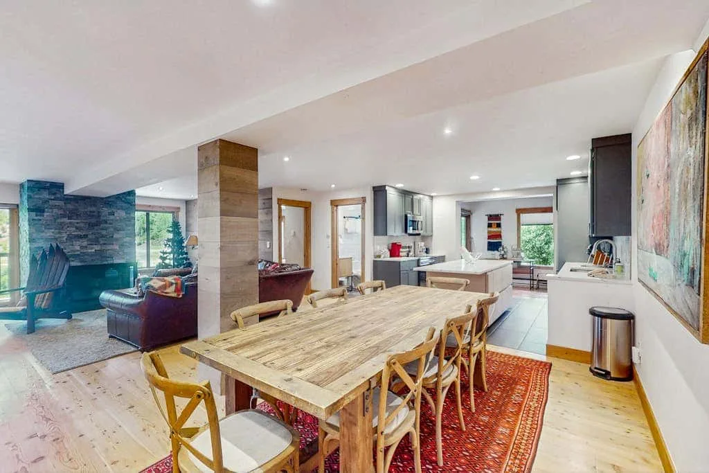 An open-plan dining and kitchen area features a long wooden table and red rug.