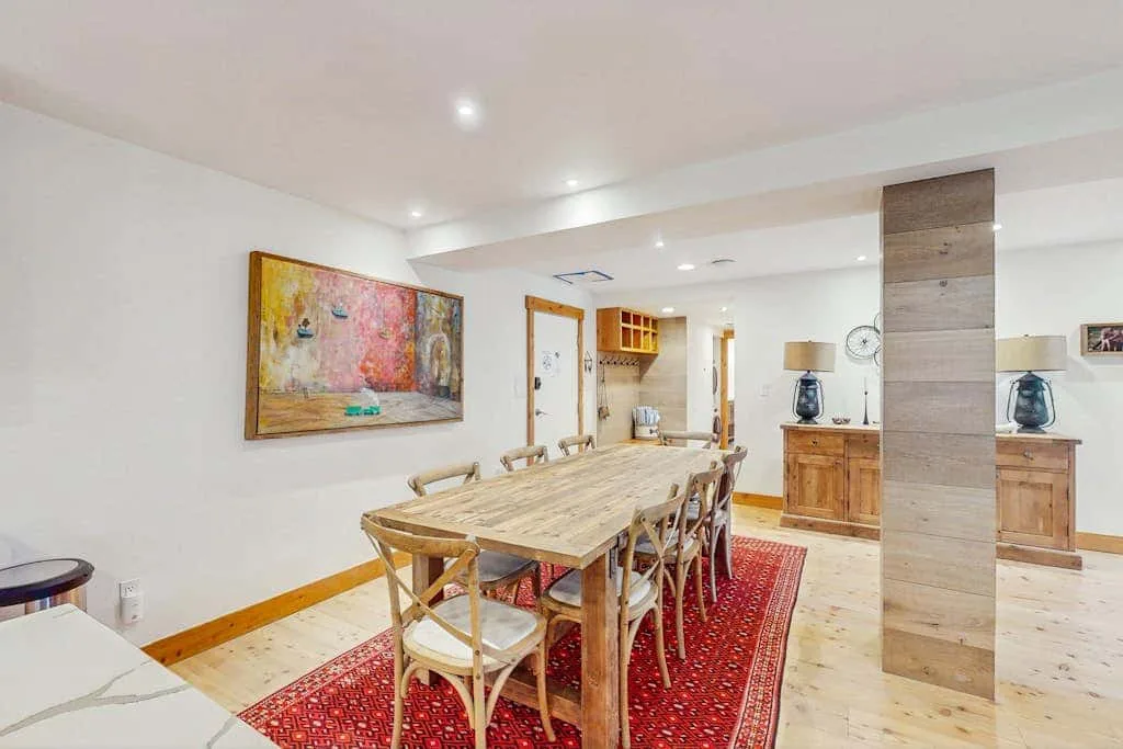 A dining area with a long wooden table and chairs on a patterned rug.