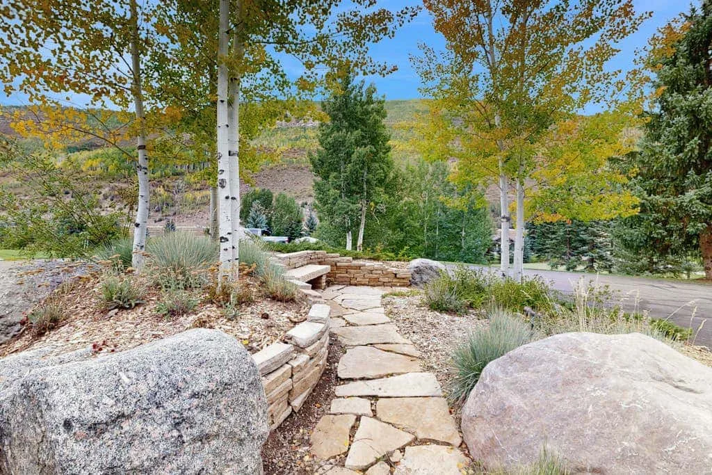 A stone garden path winds through landscaped grounds beneath leafy trees.
