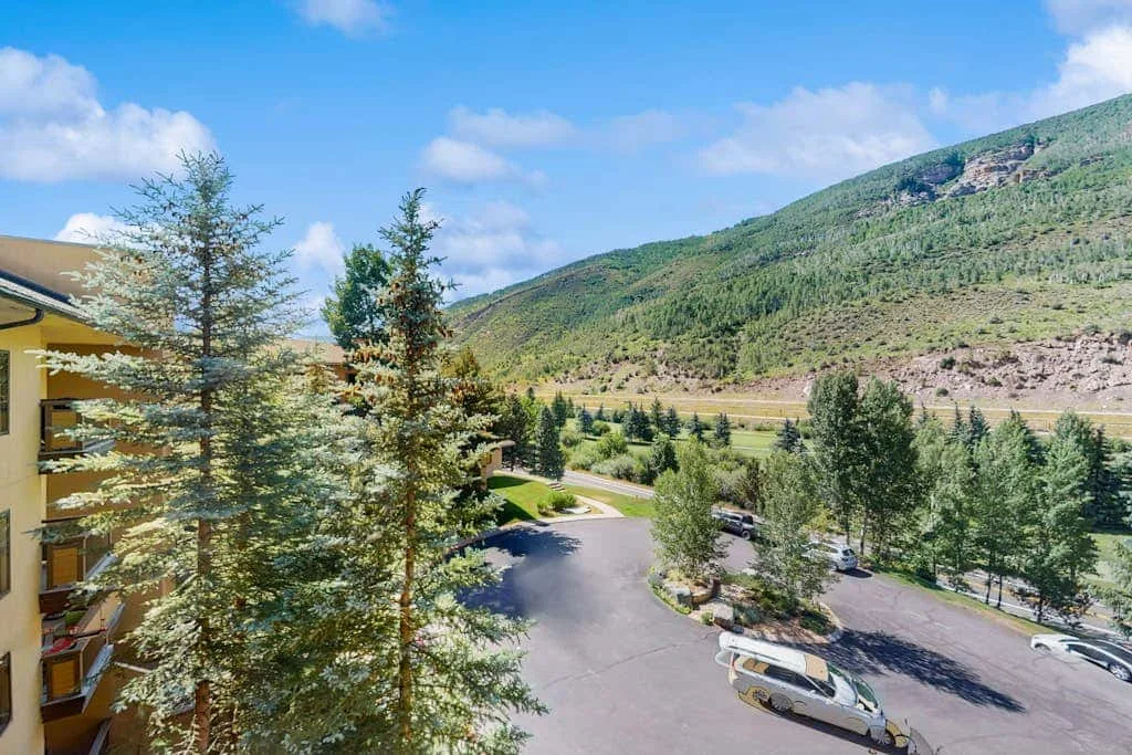 A mountain valley with trees, a winding road, and parked vehicles.