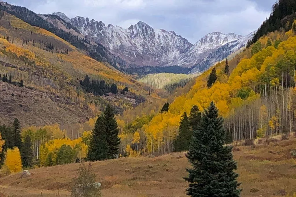 An autumn mountain valley with colorful forested slopes beneath snow-dusted peaks.