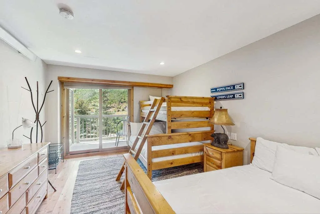 A bedroom with wooden bunk beds, a large bed, and sliding glass doors.