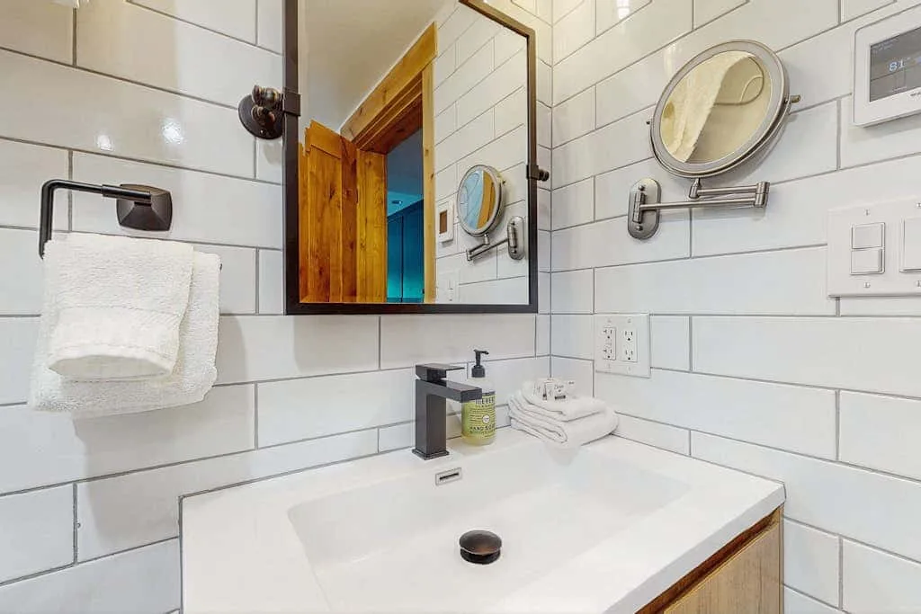 A bright tiled bathroom with a sink, mirror, and neatly folded towels.