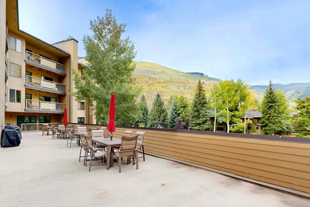 An outdoor terrace with patio seating overlooks trees and a mountain landscape.