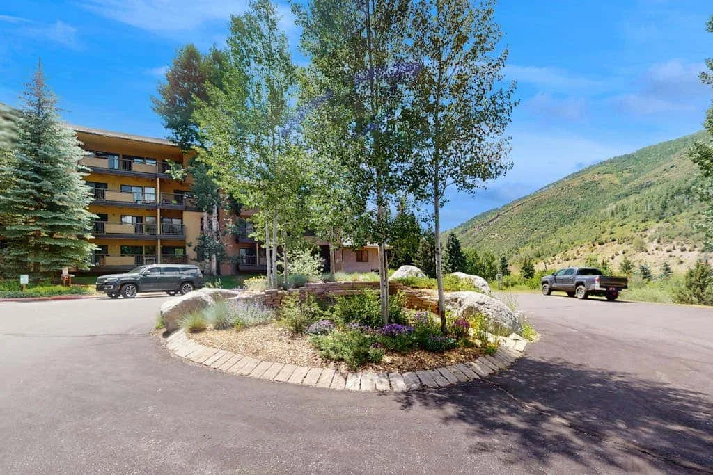 A mountain-side building stands beside a paved parking area and landscaped island.