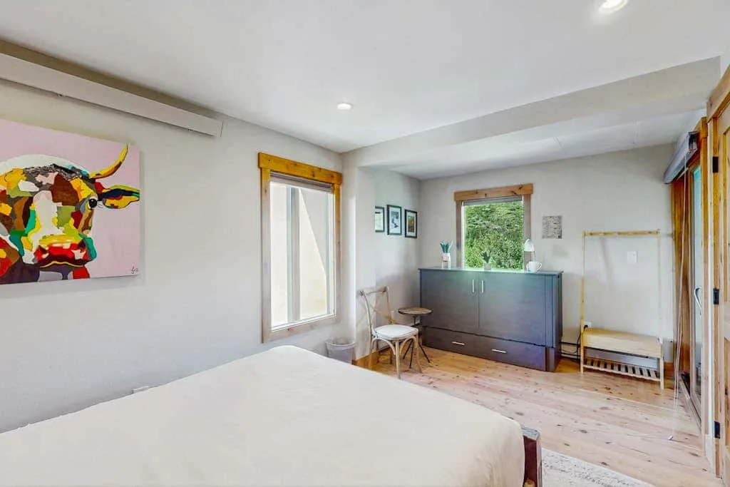 A bright bedroom with a bed, colorful wall art, and a dark dresser.