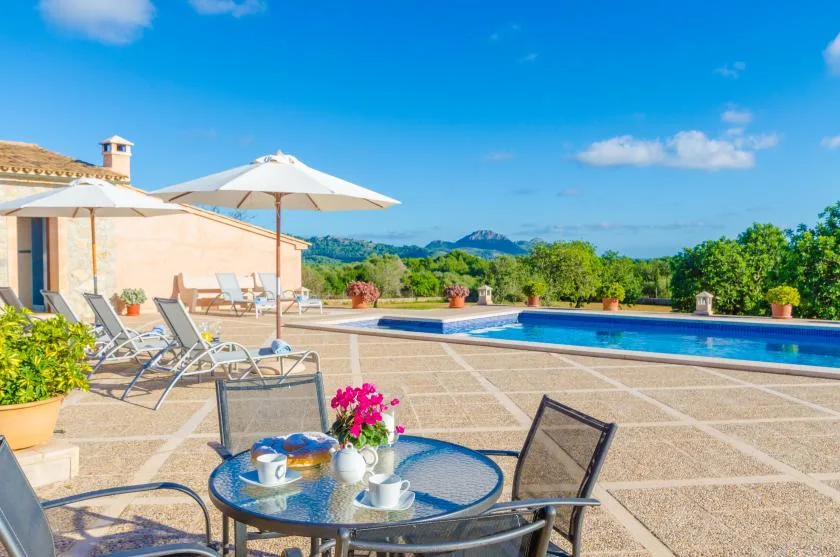 A sunny patio with outdoor seating, umbrellas, and a swimming pool.