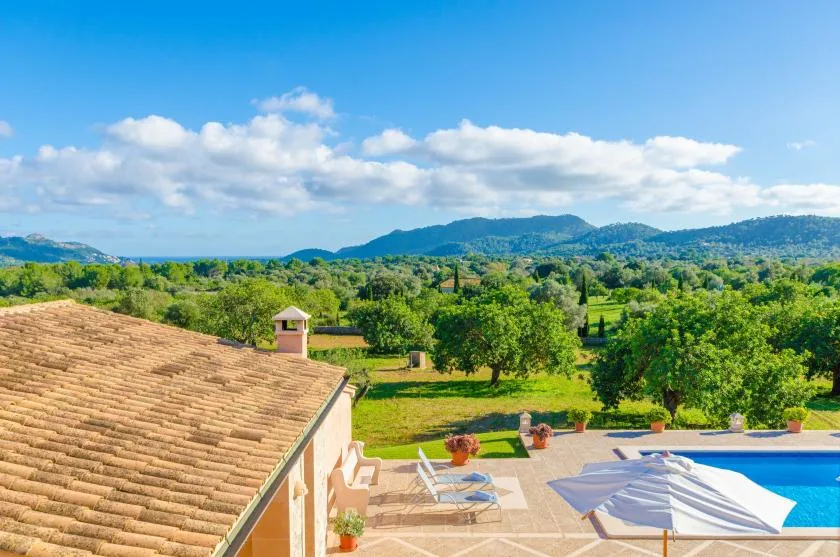 A swimming pool and patio overlook a green landscape and distant hills.