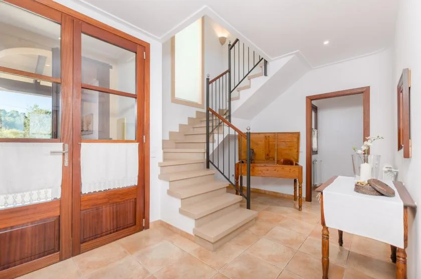 A bright interior hall with a staircase, wooden doors, and a small table.