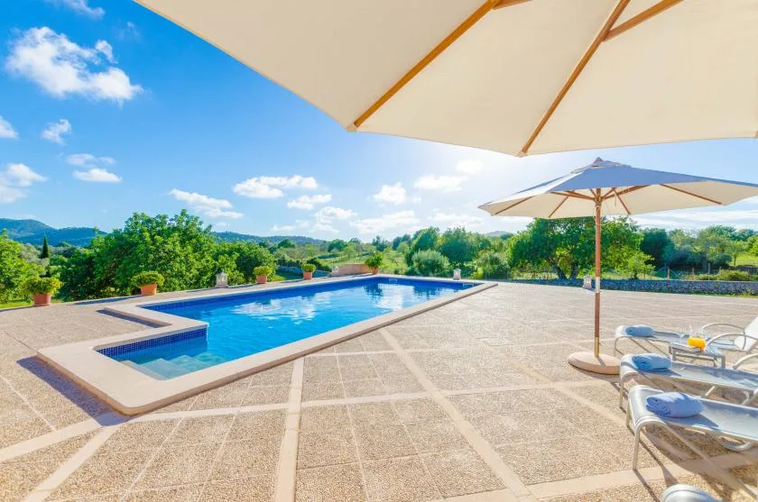A swimming pool and sun loungers sit on a broad patio beneath umbrellas.