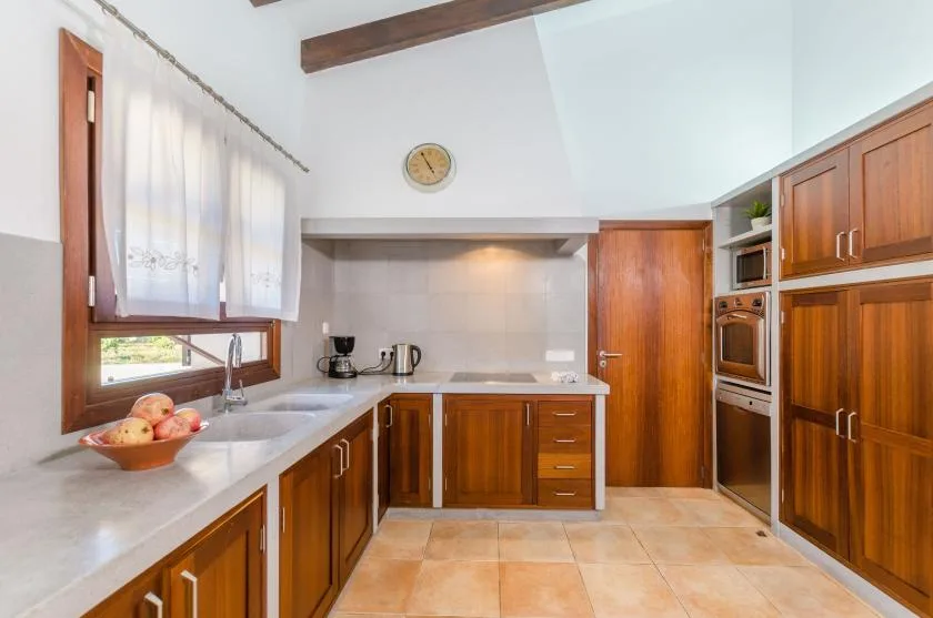 A kitchen with wooden cabinets, a countertop, and a window with sheer curtains.