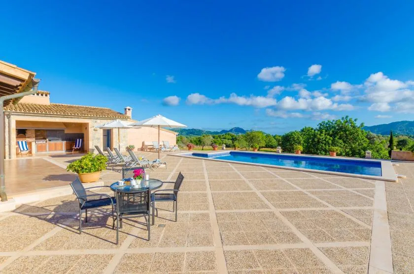 A sunny outdoor patio with seating beside a long swimming pool.