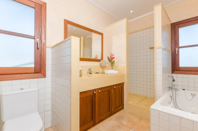 A tiled bathroom with a wooden vanity, mirror, and bathtub.