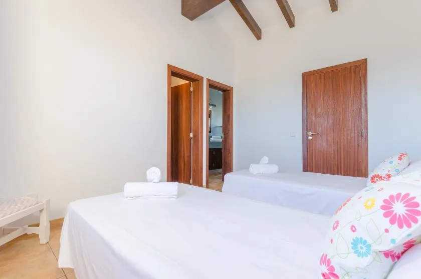 A bright bedroom with two beds and exposed wooden ceiling beams.