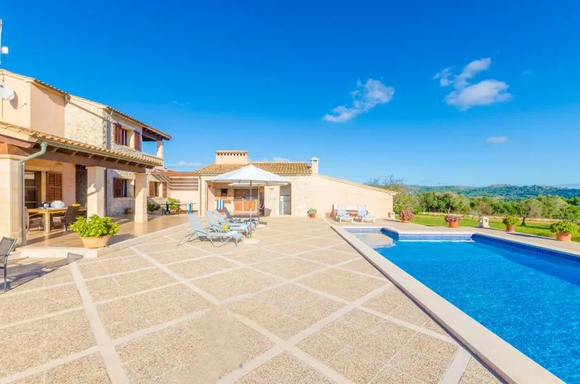 A spacious outdoor patio beside a swimming pool, with seating and a clear blue sky.