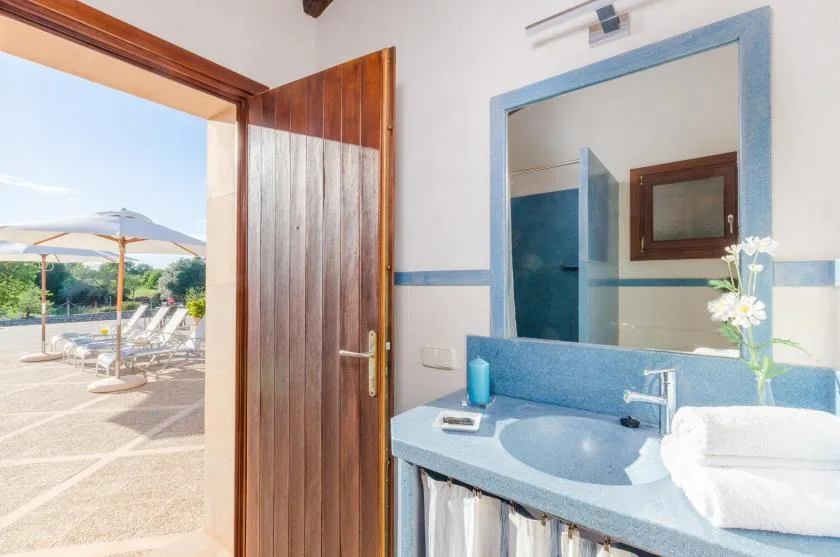 A bathroom vanity with a large mirror sits beside an open wooden door to a patio.