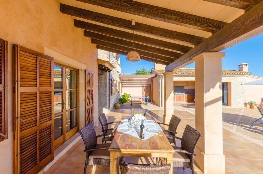 A covered outdoor dining area with a long table and chairs beside the house.
