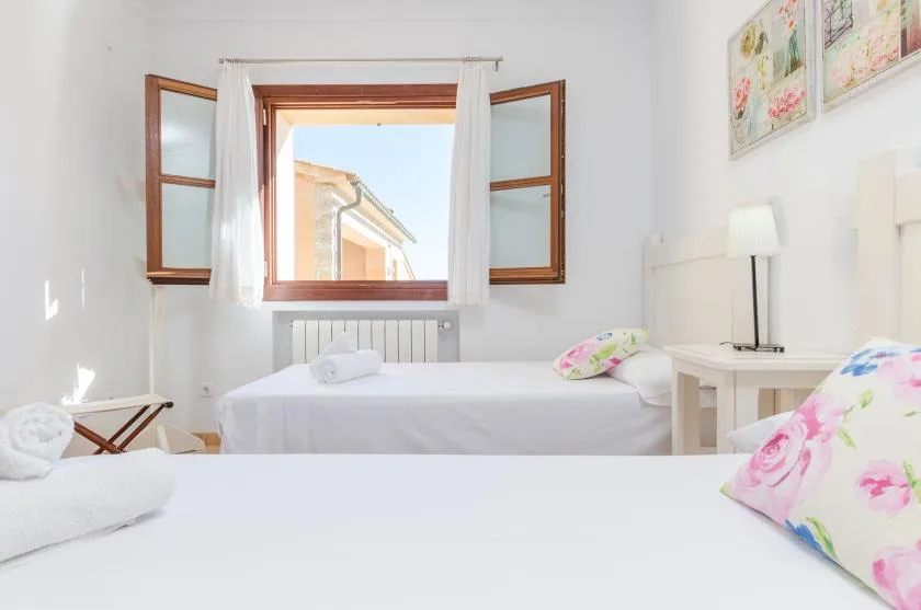 A bright bedroom with white bedding and an open window.