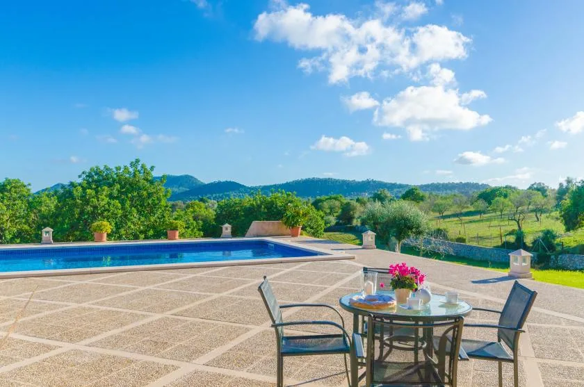 An outdoor poolside terrace with a table and seating overlooking green hills.