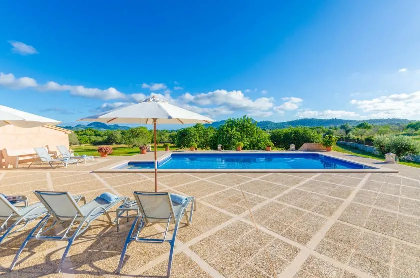 A swimming pool and outdoor seating overlook green fields beneath a clear blue sky.