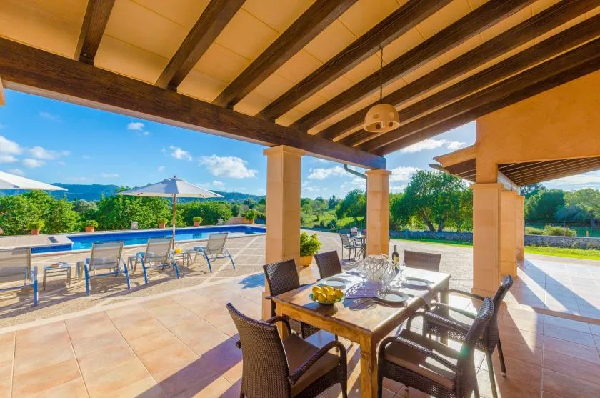 A covered outdoor dining area opens onto a patio beside a swimming pool.
