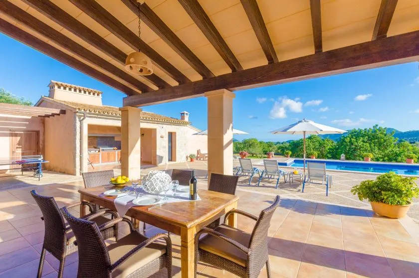 A covered patio dining area overlooks a swimming pool and garden.