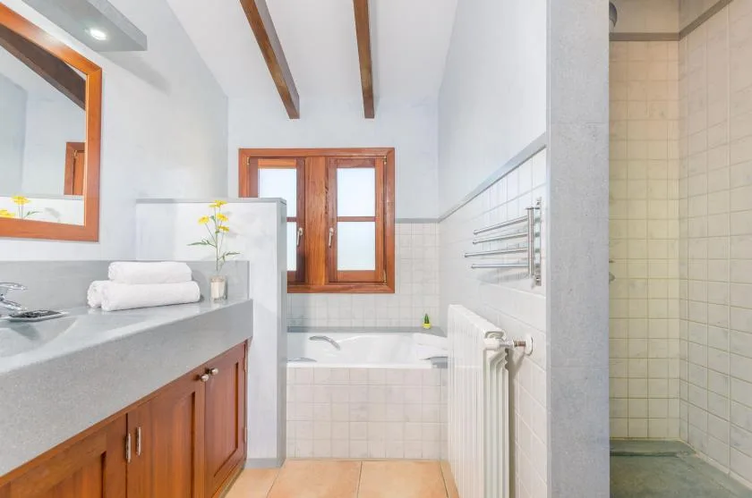 A bright bathroom with a bathtub beneath a wooden-framed window.