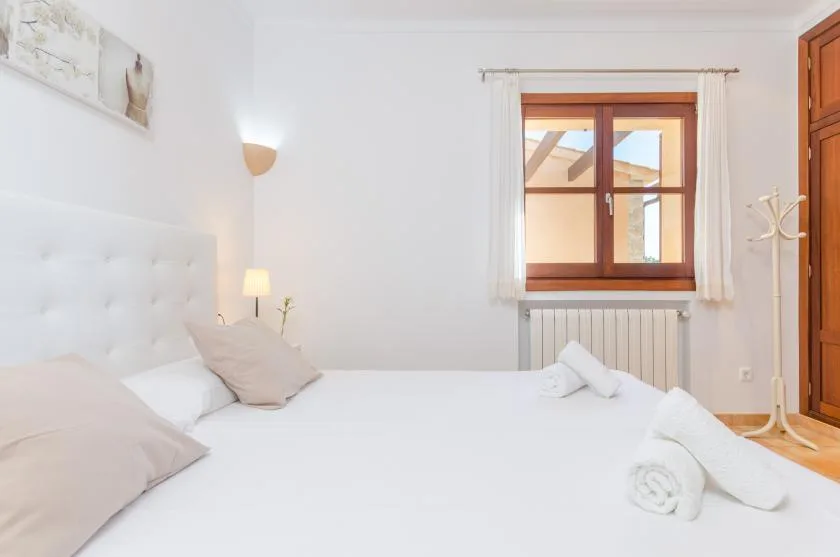 A bright bedroom with a bed beneath a wood-framed window.