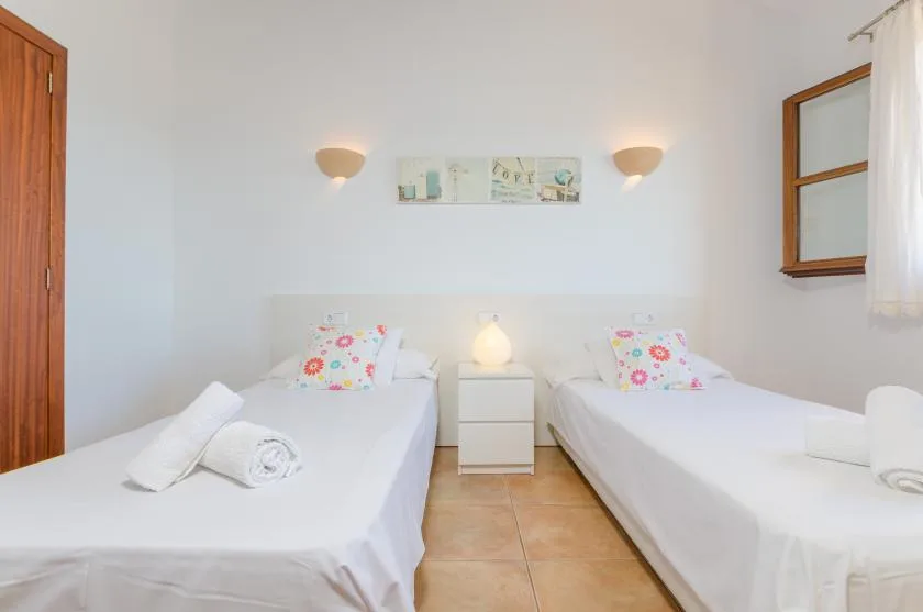 A bedroom with two single beds, bedside table, and wall sconces.
