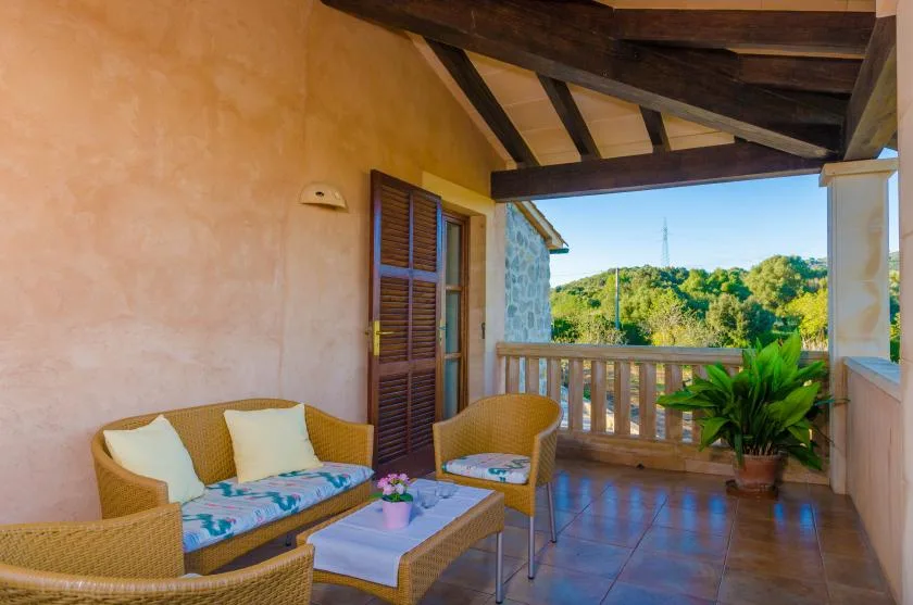A covered terrace with wicker seating and a view of green hills.