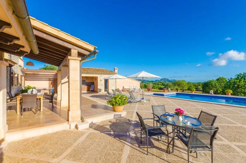 A sunny outdoor patio with dining furniture beside a swimming pool.