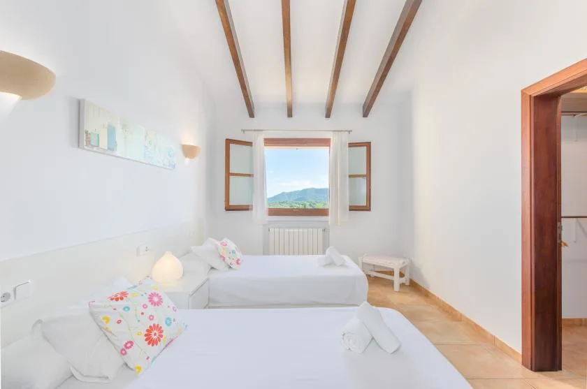 A bright bedroom with white bedding, exposed ceiling beams, and a window overlooking hills.