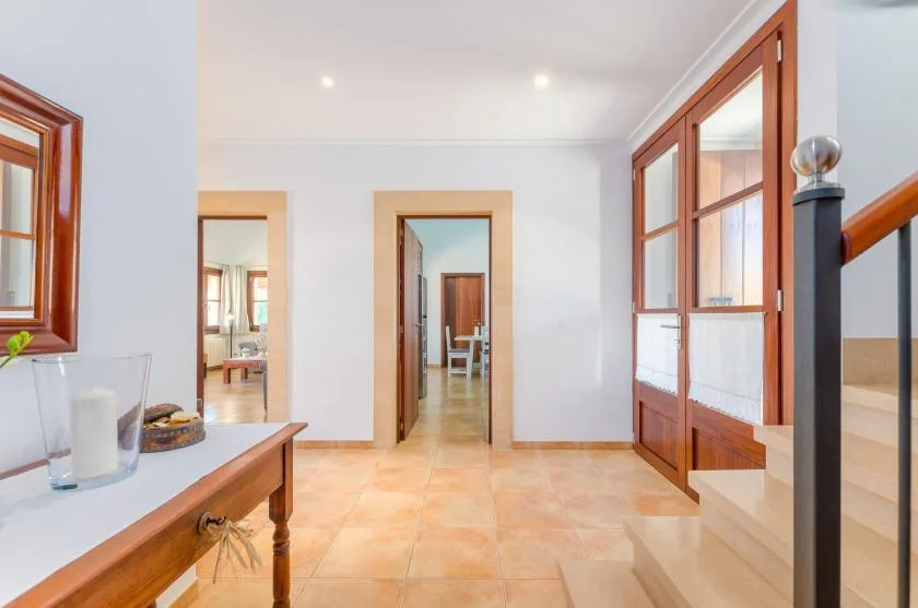 A bright tiled hallway connects several open doorways, with a wooden table beside the window.