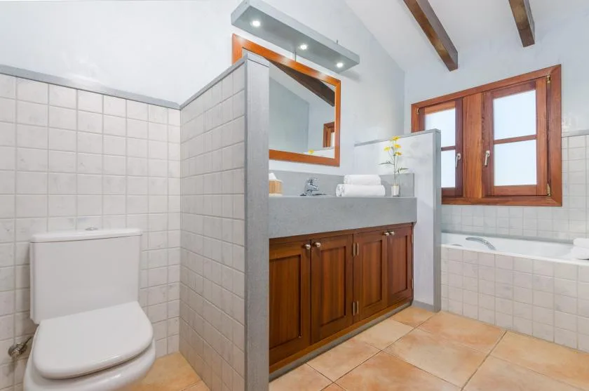 A tiled bathroom with a vanity, toilet, and bathtub beneath a window.