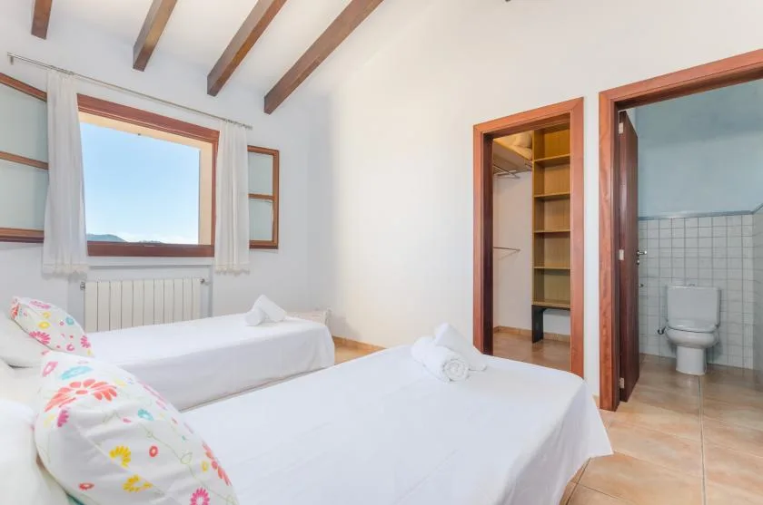 A bedroom with two beds, a window, and an open doorway to a bathroom.