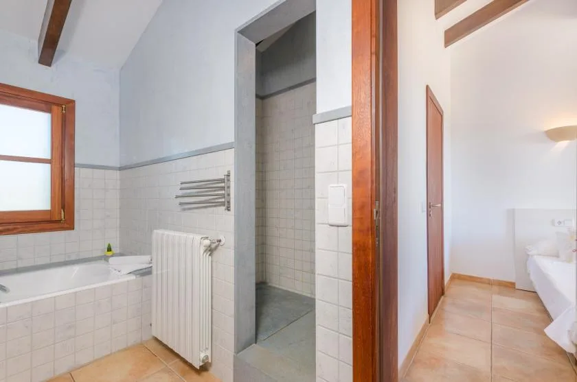 A tiled bathroom with a bathtub, radiator, and open shower area.