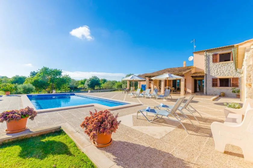 An outdoor pool and paved patio sit beside a stone-faced house.