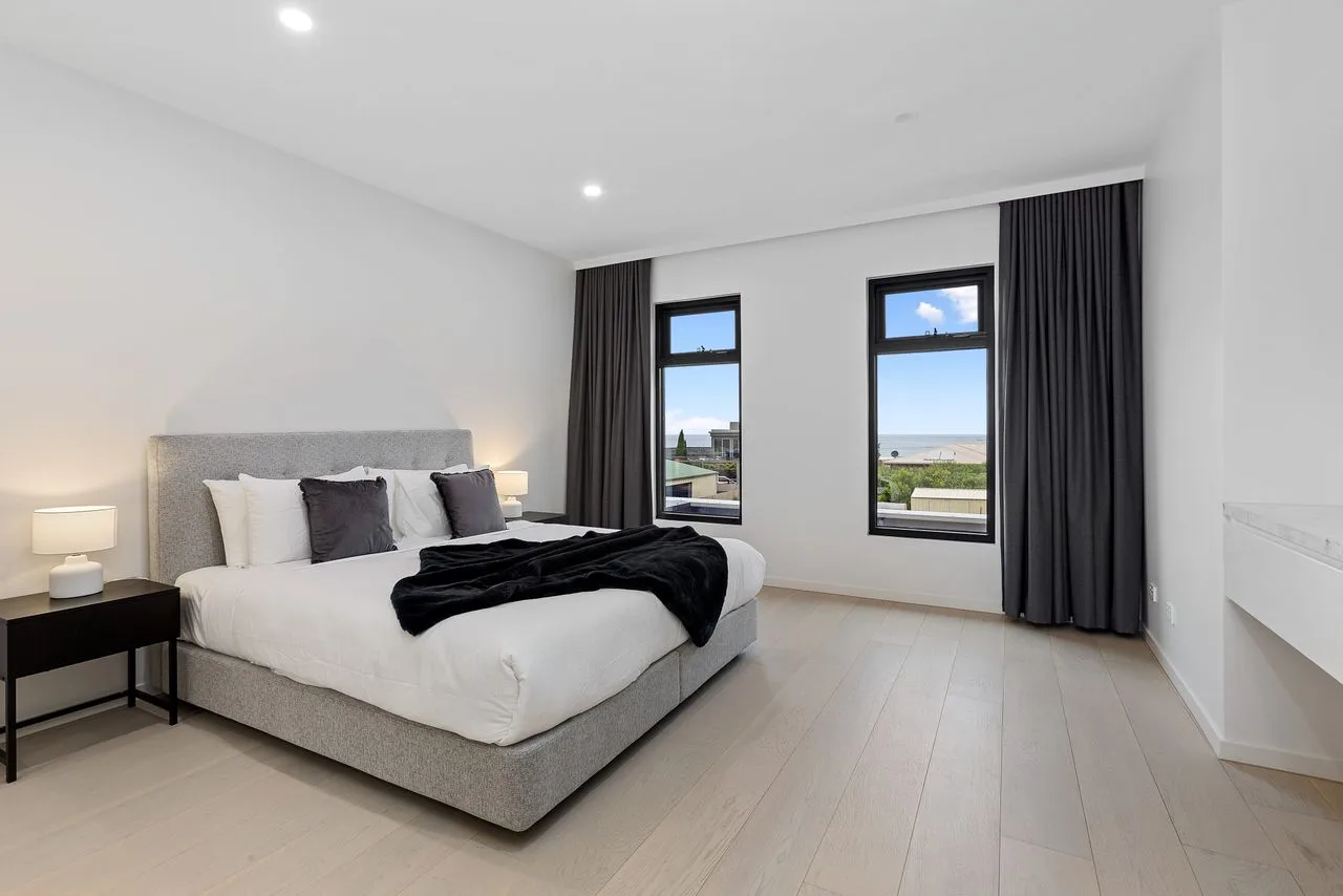 Un dormitorio luminoso con una cama tendida y cortinas oscuras.